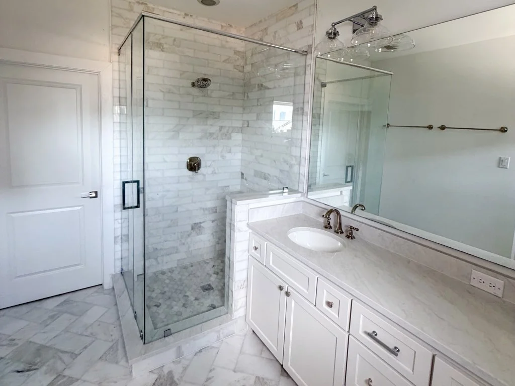 Bathroom with marble subway tile shower, frameless glass enclosure, herringbone marble floor, and white shaker vanity with marble countertop