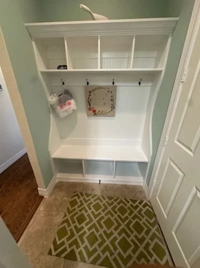 White built-in shelving unit with open shelves, hooks, and lower storage bench in entryway