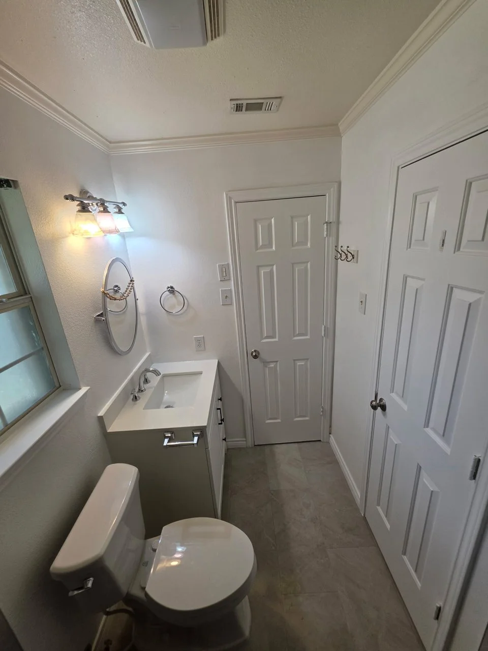 Bathroom with white quartz vanity, undermount sink, gray large-format floor tile, white six-panel doors, and crown molding