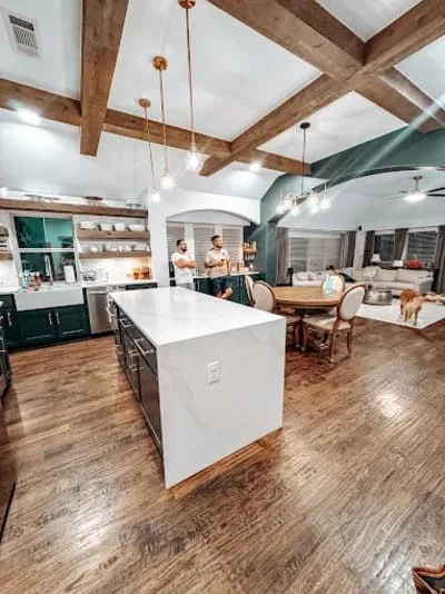 Open kitchen with white island, teal cabinetry, exposed beams, hardwood floors, and pendant lighting