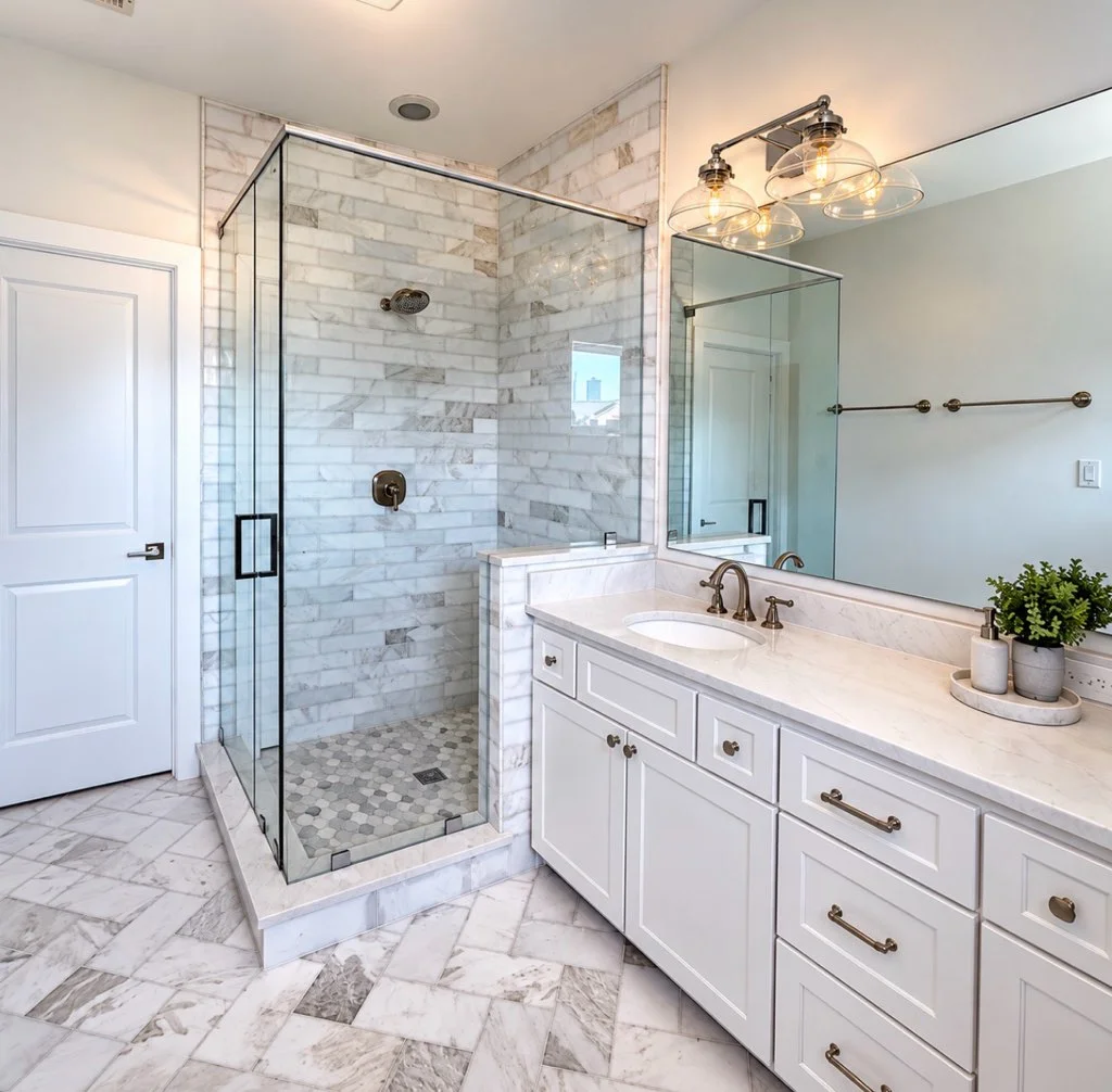 Bathroom with marble subway tile shower, frameless glass enclosure, hex mosaic shower floor, white shaker vanity with bronze hardware