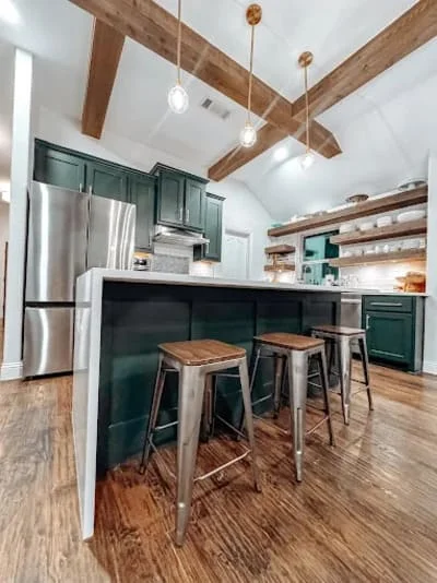 Kitchen with dark green cabinets, exposed wood beams, white tile backsplash, and wood bar seating