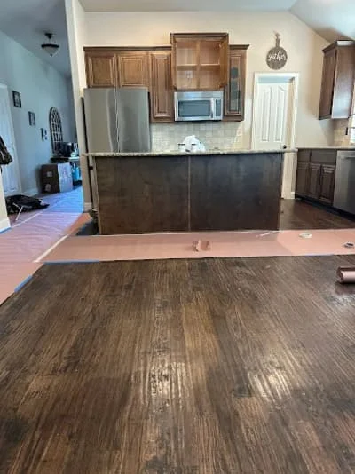 Wood-look flooring installation in kitchen and living area with new cabinetry and stainless steel appliances