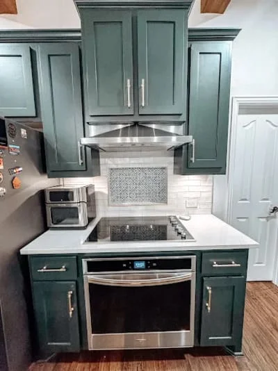 Teal kitchen cabinets with stainless steel appliances, white countertops, and tile backsplash